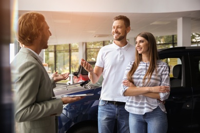 Photo of Salesman with tablet consulting young couple in car dealership