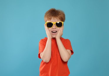 Photo of Cute little boy with sunglasses on light blue background