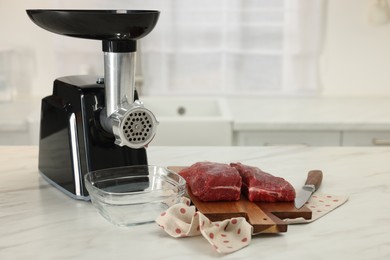 Photo of Electric meat grinder with beef and knife on white marble table in kitchen