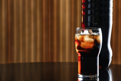 Photo of Glass of cola with ice and bottle on table against blurred background. Space for text