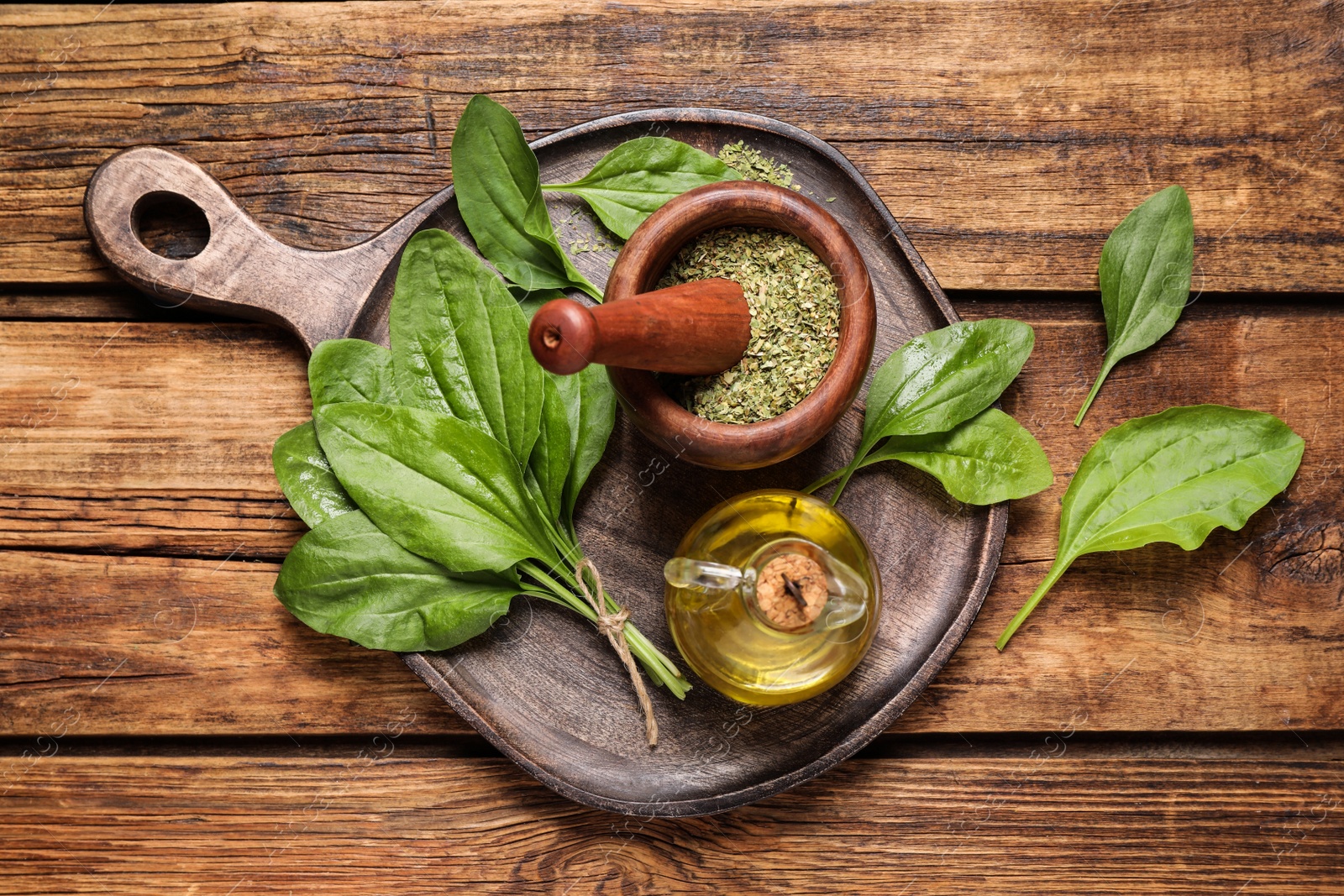 Photo of Fresh and dried broadleaf plantain leaves with essential oil on wooden table, flat lay