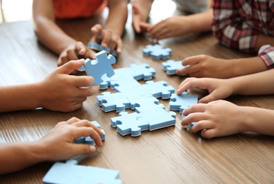 Photo of Little children playing with puzzle at table, focus on hands. Unity concept