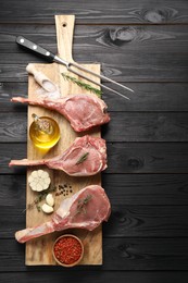 Photo of Fresh tomahawk beef cuts, spices and butcher fork on black wooden table, top view