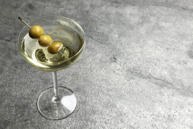 Photo of Martini cocktail with olives on grey table. Space for text