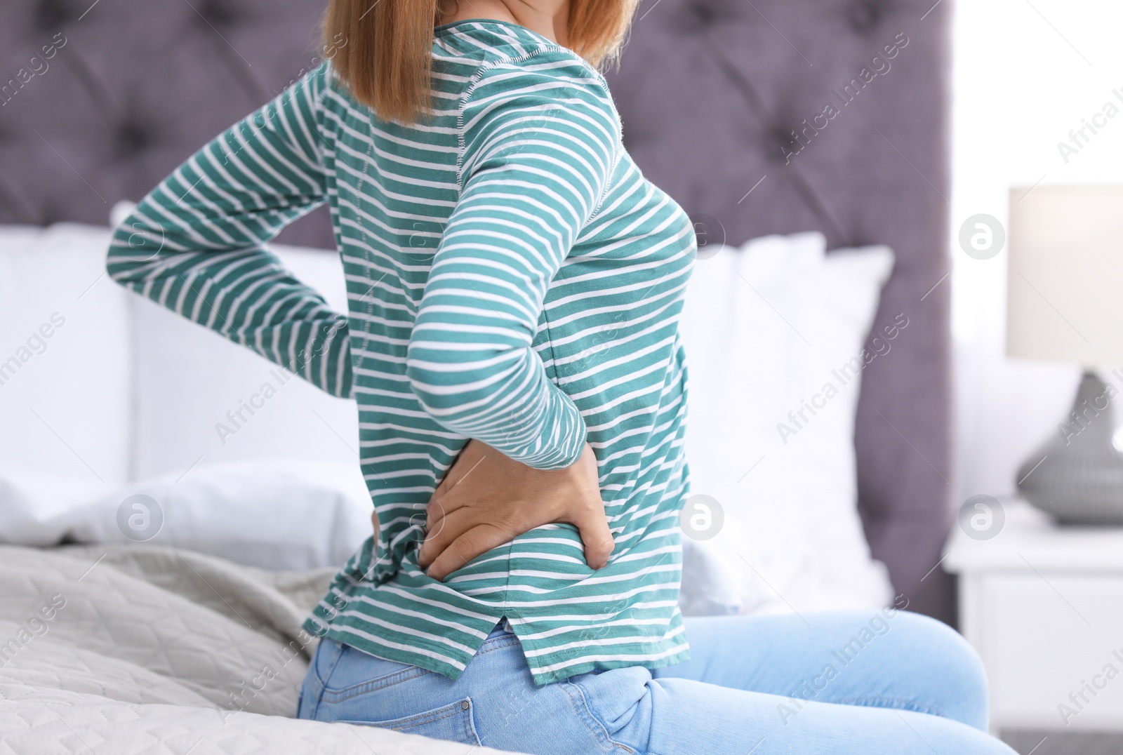 Photo of Young woman suffering from back pain at home, closeup