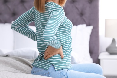 Young woman suffering from back pain at home, closeup