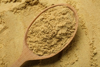 Photo of Heap of aromatic mustard powder and wooden spoon, top view