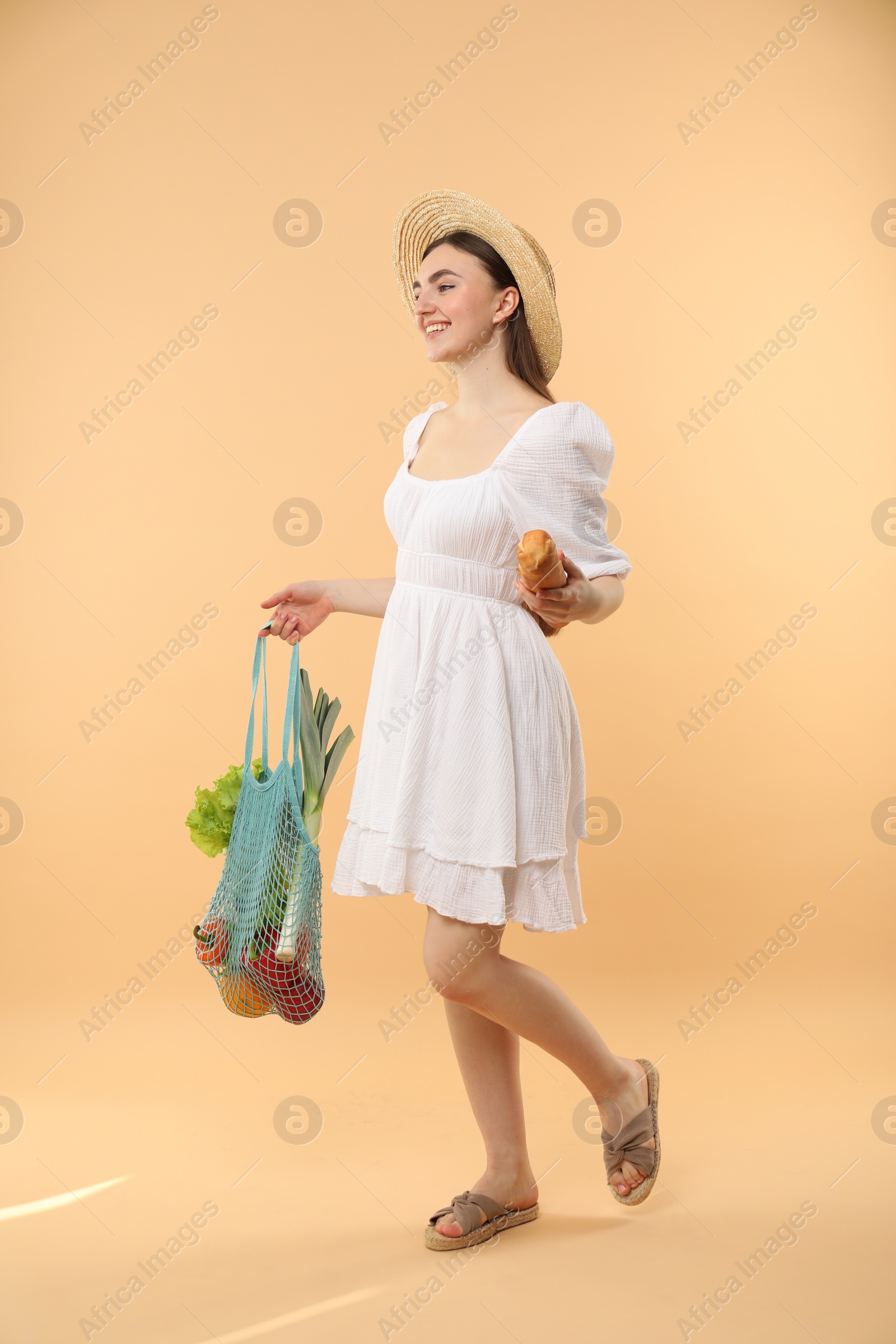 Photo of Woman with string bag of fresh vegetables and baguette on beige background