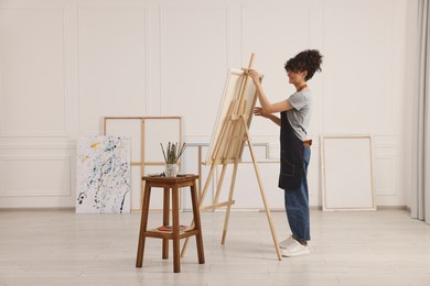 Photo of Young woman near wooden easel in studio