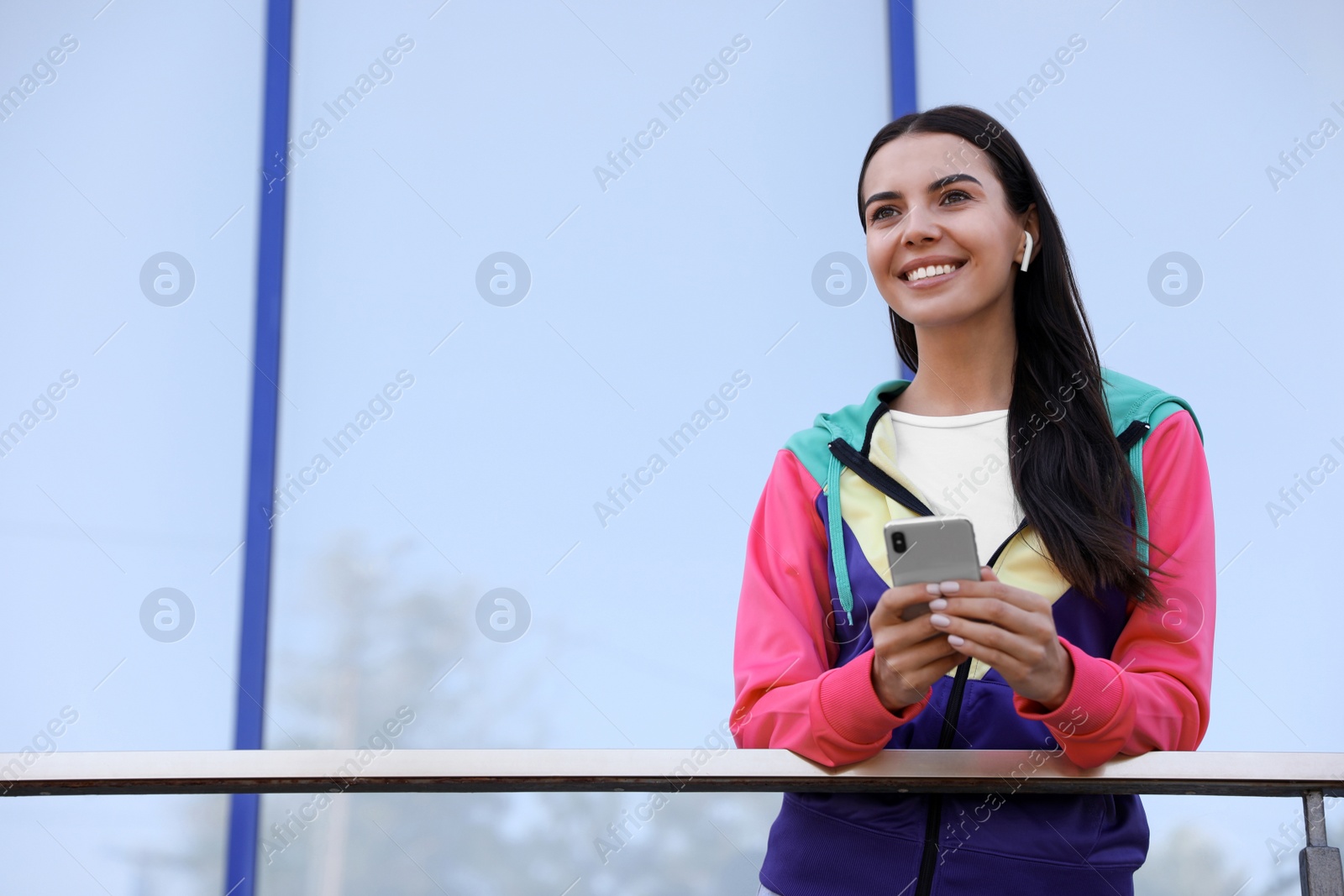 Photo of Young sportswoman with wireless earphones and smartphone on city street