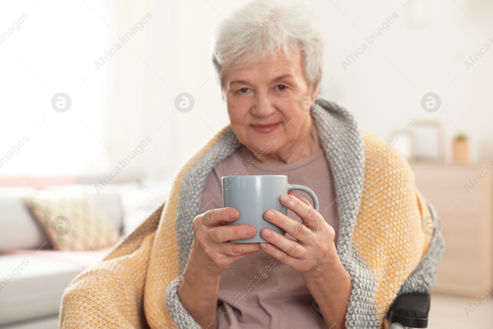 Photo of Elderly woman covered with blanket drinking tea at nursing home. Assisting senior people