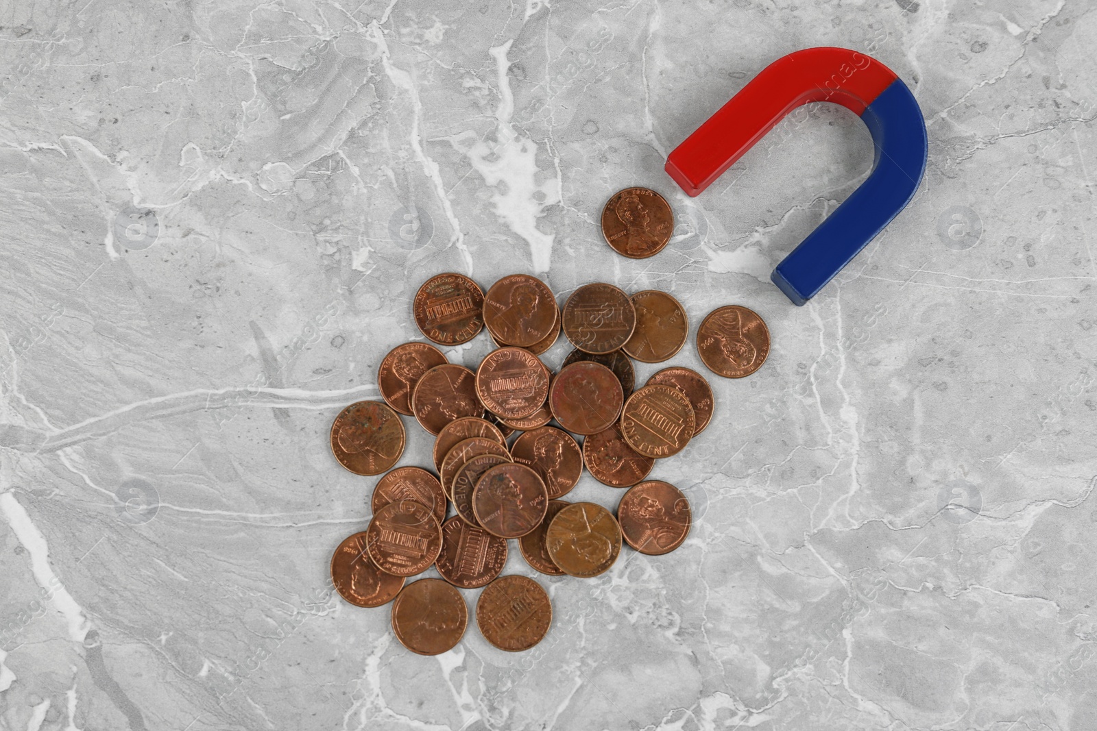 Photo of Magnet attracting coins on grey marble table, flat lay