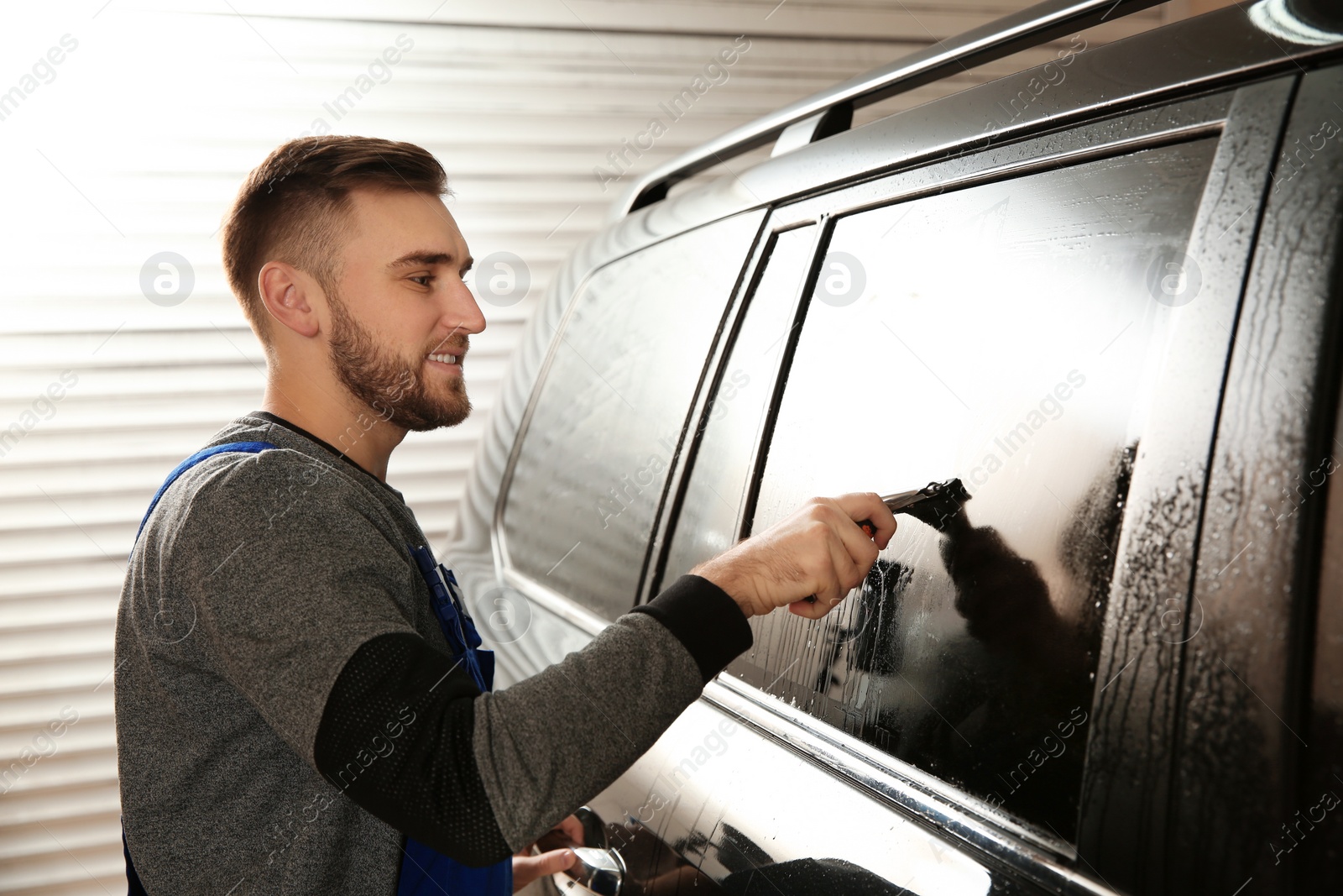 Photo of Skilled worker washing tinted car window in shop