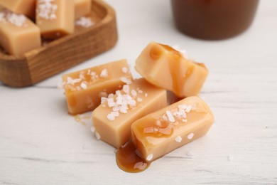 Yummy caramel candies, sauce and sea salt on white wooden table, closeup