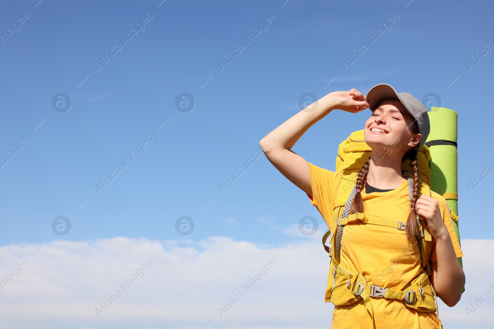 Photo of Young woman with backpack and sleeping mat against blue sky. Space for text