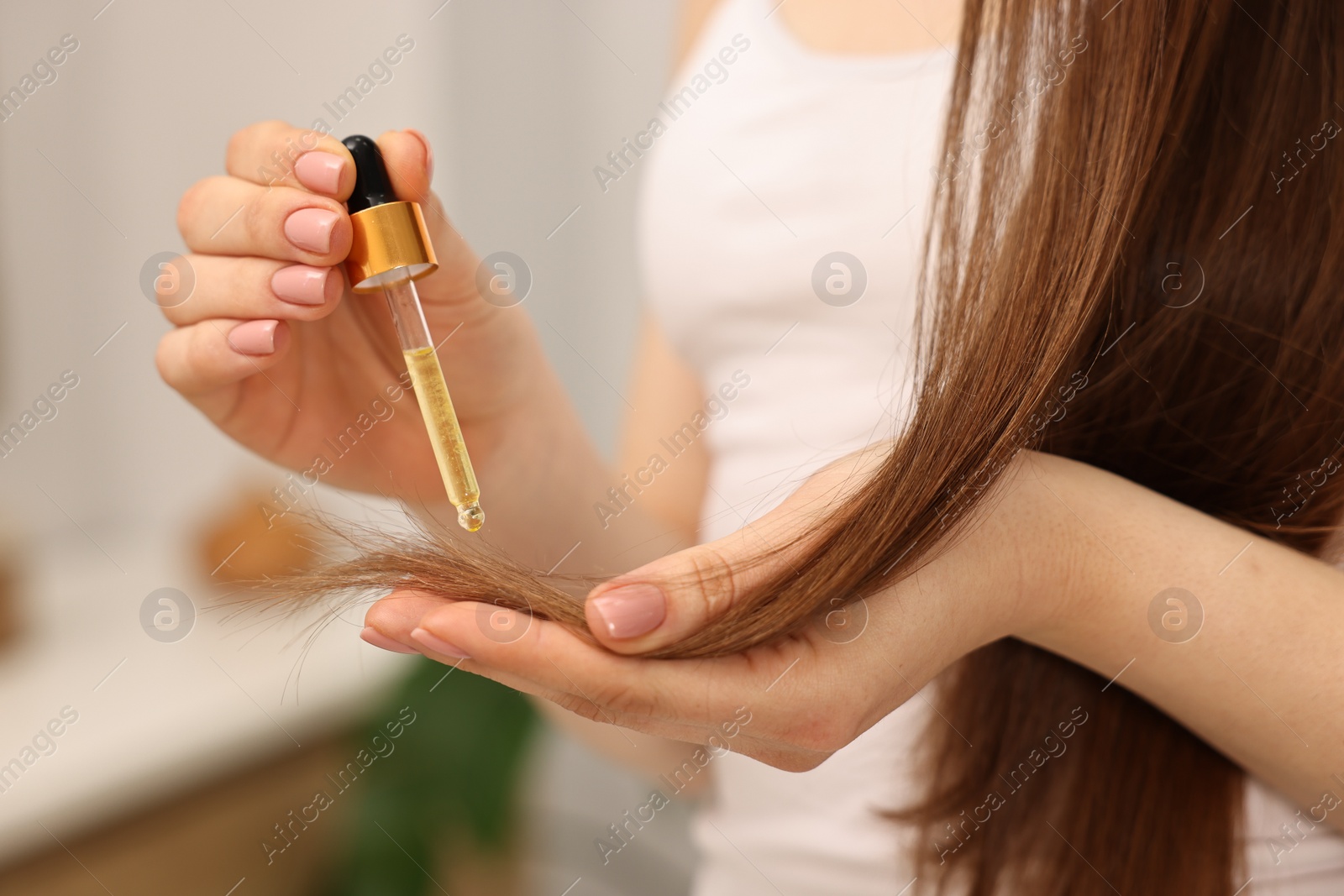 Photo of Woman applying oil hair mask indoors, closeup