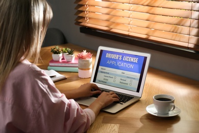 Woman using laptop to fill driver's license application form at table in office, closeup