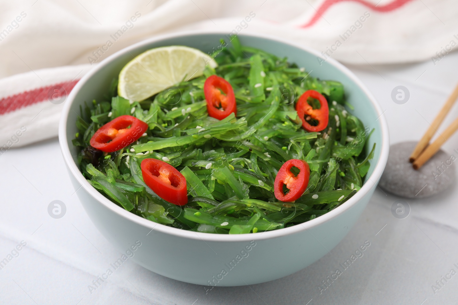 Photo of Tasty seaweed salad in bowl served on white table, closeup