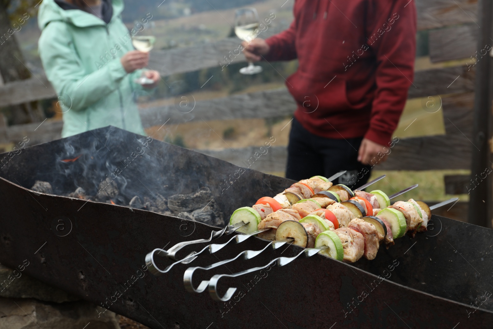 Photo of Couple having barbecue party outdoors, focus on brazier with meat and vegetables