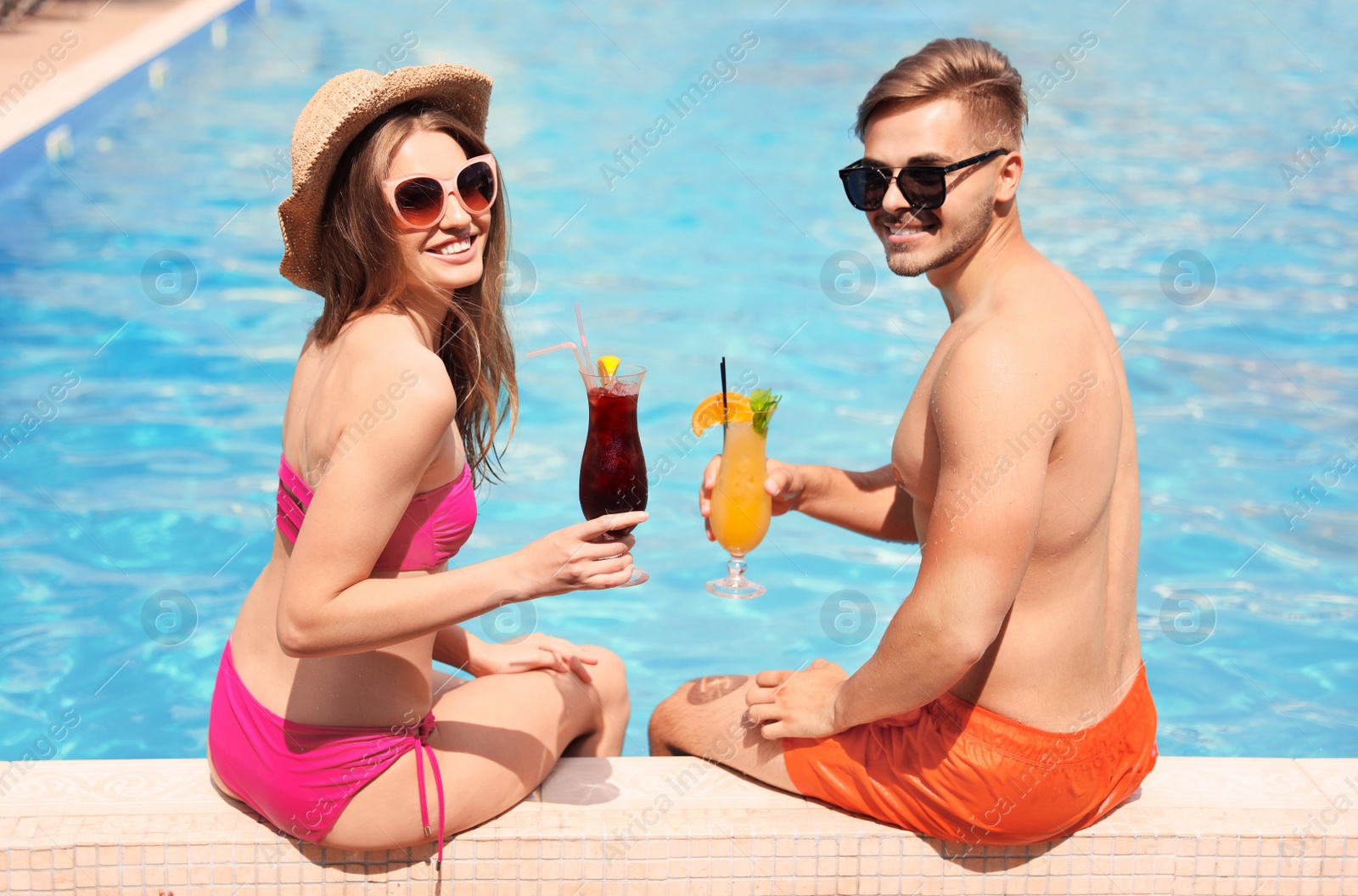 Photo of Young couple with cocktails near pool on sunny day