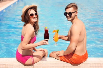 Young couple with cocktails near pool on sunny day