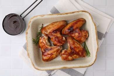 Photo of Fresh marinade, chicken wings and rosemary on white tiled table, top view