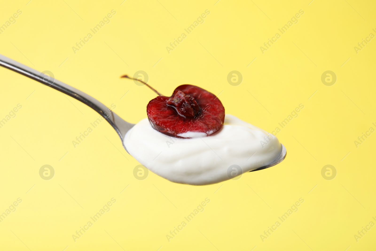 Photo of Spoon with yogurt and cherry on yellow background, closeup