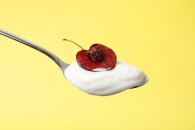 Photo of Spoon with yogurt and cherry on yellow background, closeup