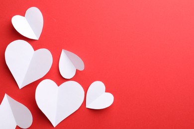 White paper hearts on red background, flat lay. Space for text