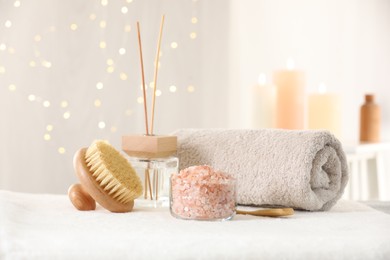 Photo of Spa composition. Sea salt, brush, towel and reed air freshener on soft white surface