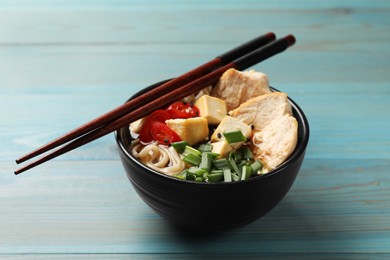 Photo of Delicious ramen and chopsticks on light blue wooden table. Noodle soup