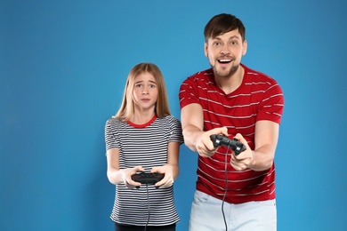 Photo of Emotional man and teenage girl playing video games with controllers on color background