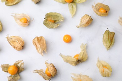 Ripe physalis fruits with calyxes on white marble table, flat lay