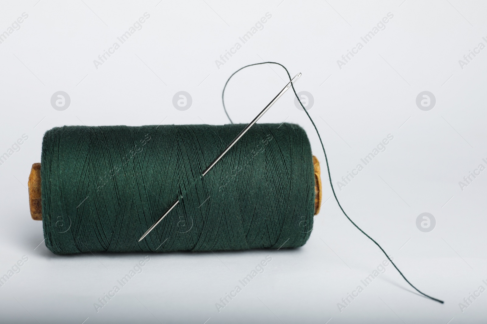 Photo of Green sewing thread with needle on white background