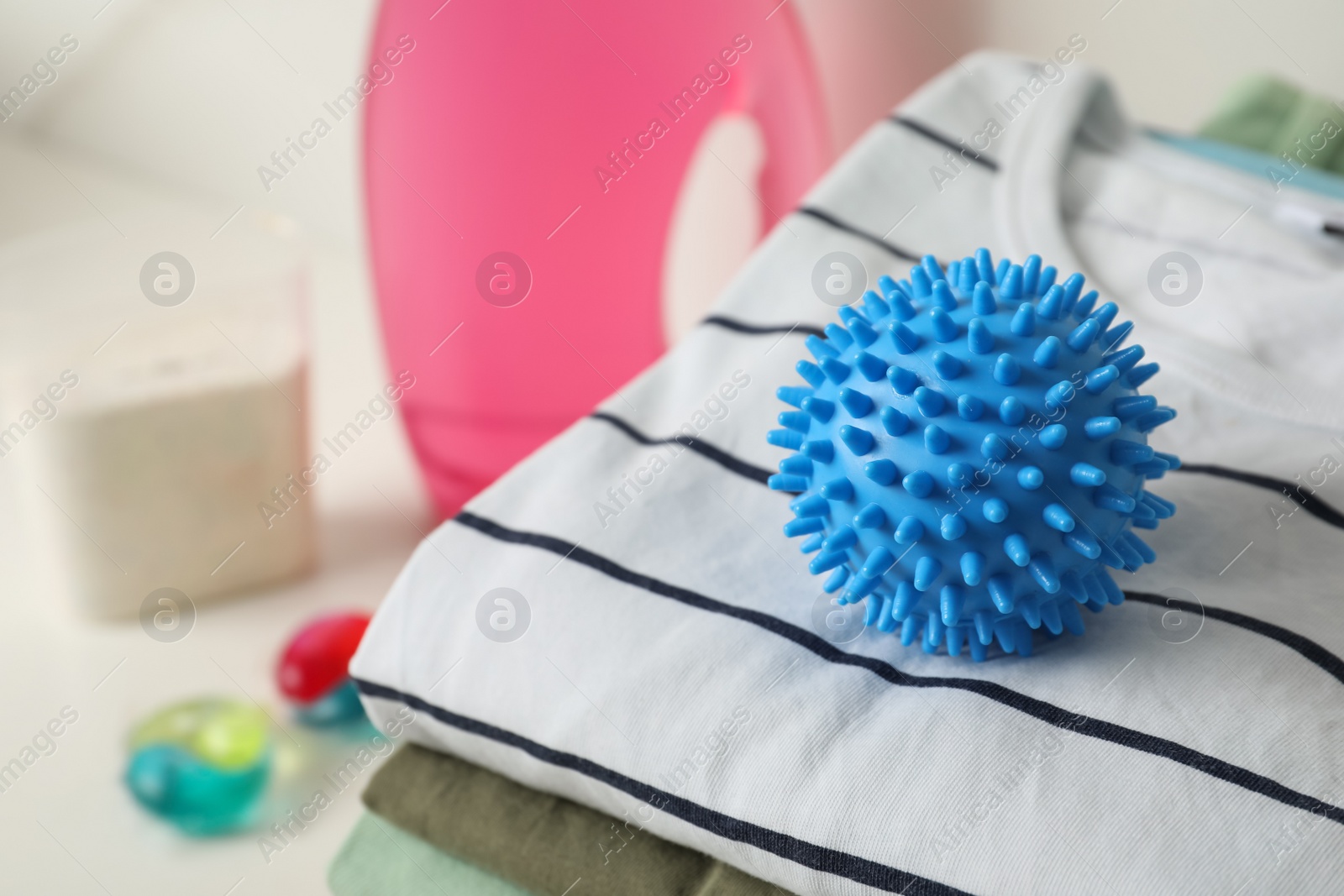 Photo of Blue dryer ball on stacked clean clothes, closeup. Space for text