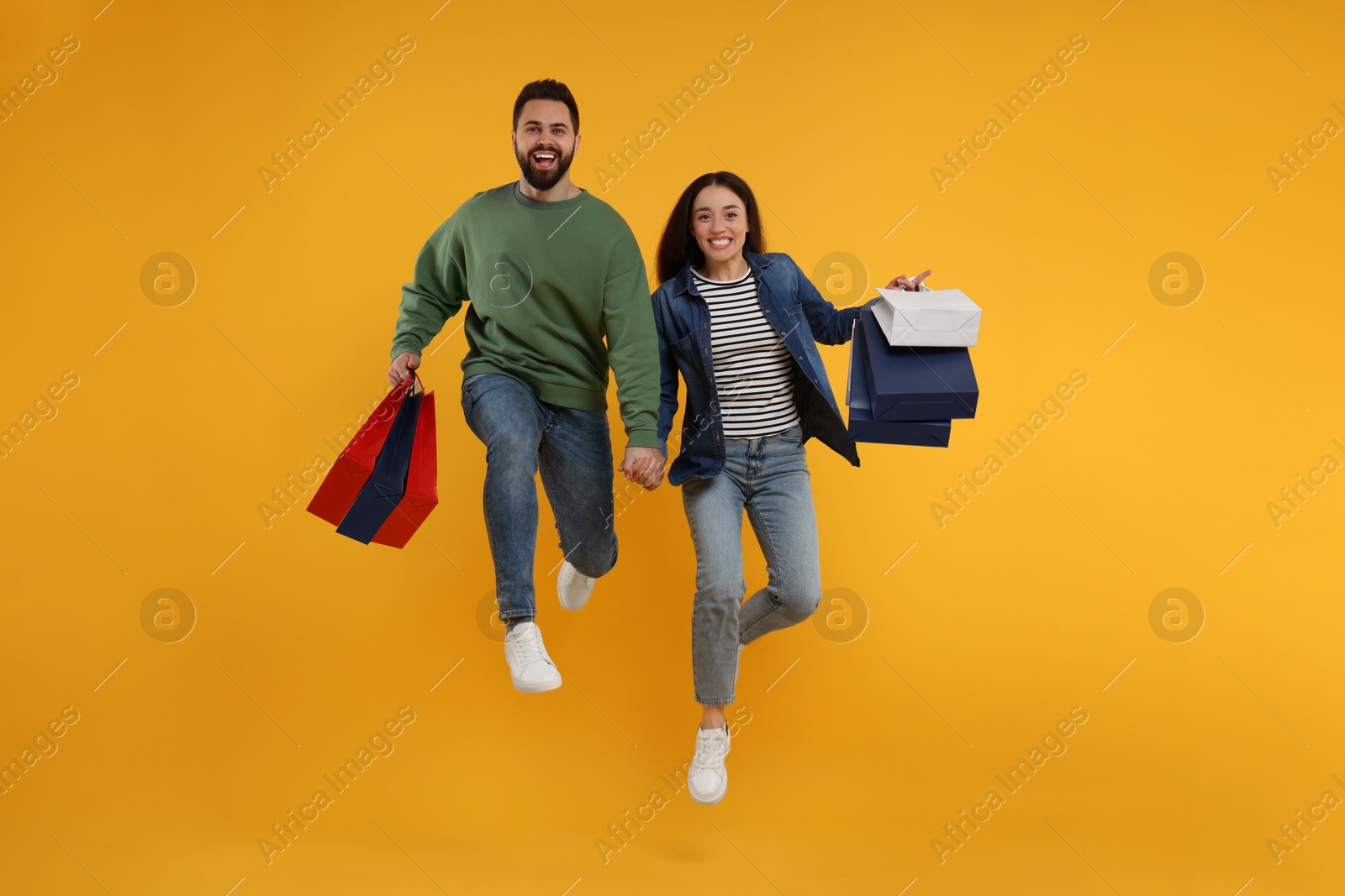 Photo of Happy couple with shopping bags jumping on orange background