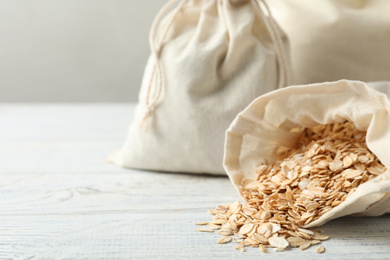 Photo of Cotton eco bags with oat flakes on white wooden table, closeup. Space for text