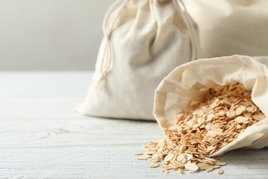 Cotton eco bags with oat flakes on white wooden table, closeup. Space for text