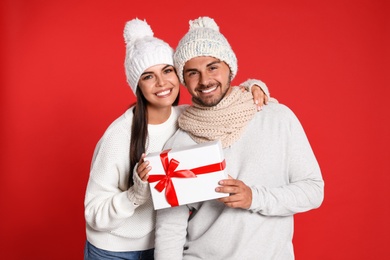 Lovely young couple with gift box on red background. Christmas celebration