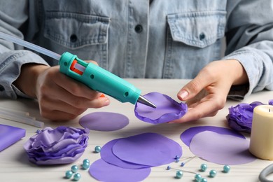 Photo of Woman with hot glue gun making craft at wooden table, closeup