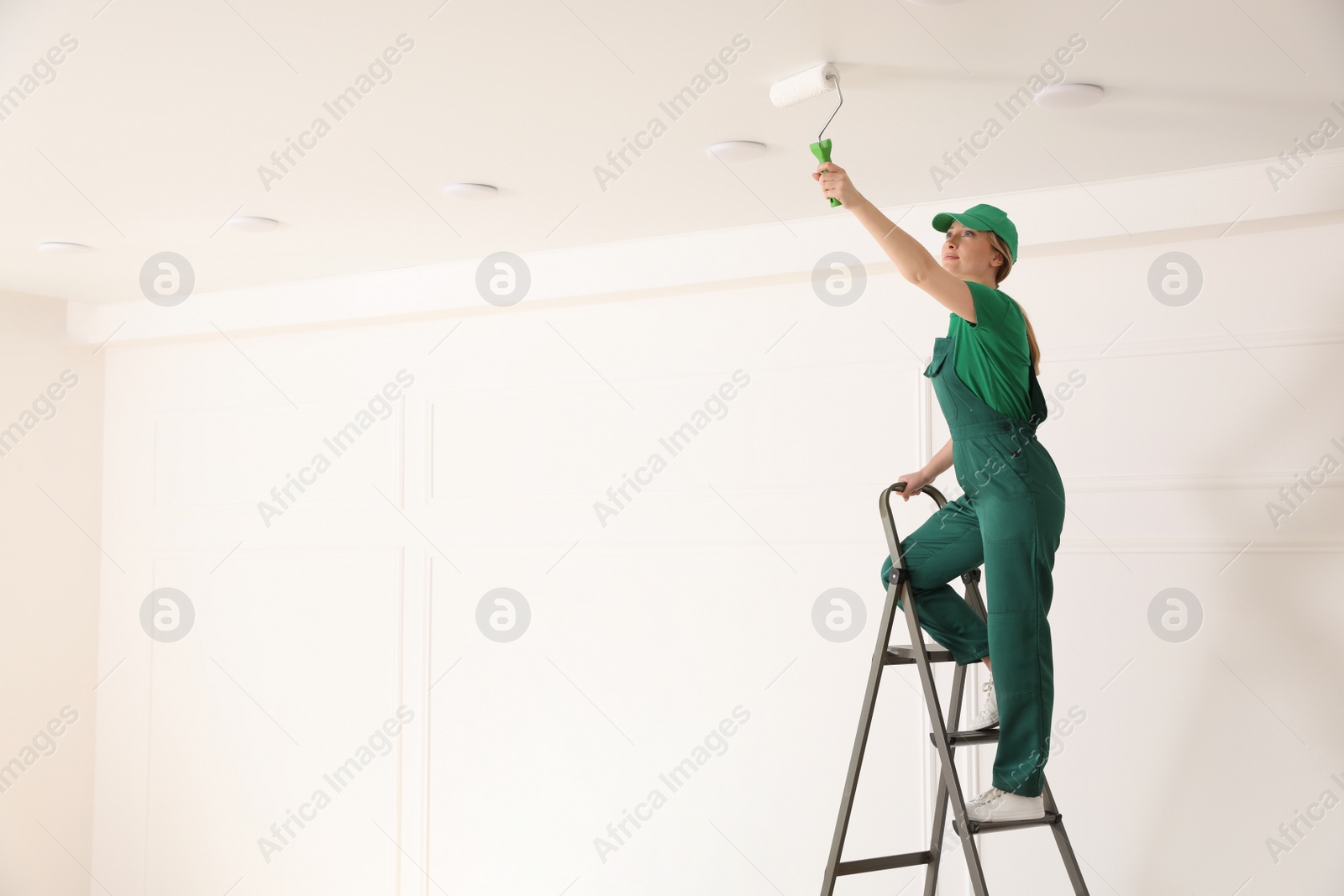 Photo of Worker painting ceiling with white dye indoors, space for text