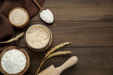 Photo of Leaven, flour, rolling pin and ears of wheat on wooden table, flat lay. Space for text