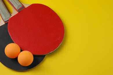 Photo of Ping pong balls and rackets on yellow background, closeup. Space for text