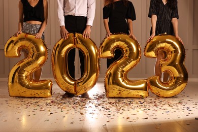 Photo of Friends with golden 2023 balloons indoors, closeup. New Year celebration