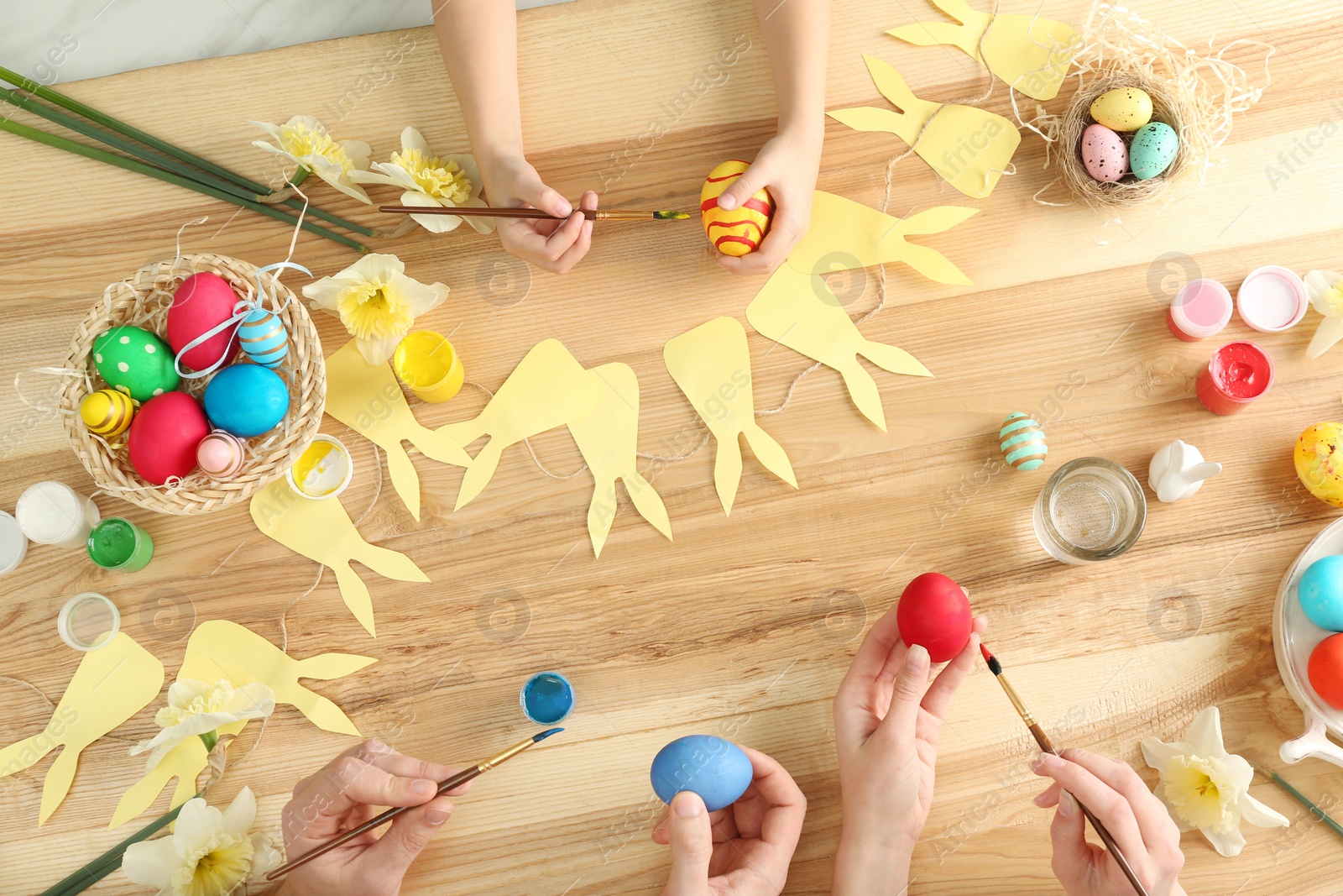 Photo of Father, mother and their child painting Easter eggs at wooden table, top view