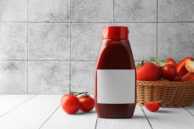 Photo of Bottle of tasty ketchup, tomatoes and pepper on white wooden table. Space for text