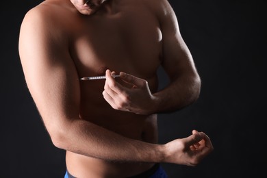 Photo of Athletic man injecting himself on black background, closeup. Doping concept