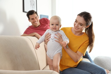 Photo of Happy parents with little baby on sofa in living room