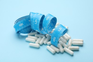 Photo of Weight loss pills and measuring tape on light blue background