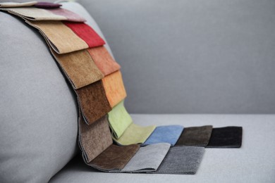 Photo of Catalog of colorful fabric samples on grey sofa. Space for text